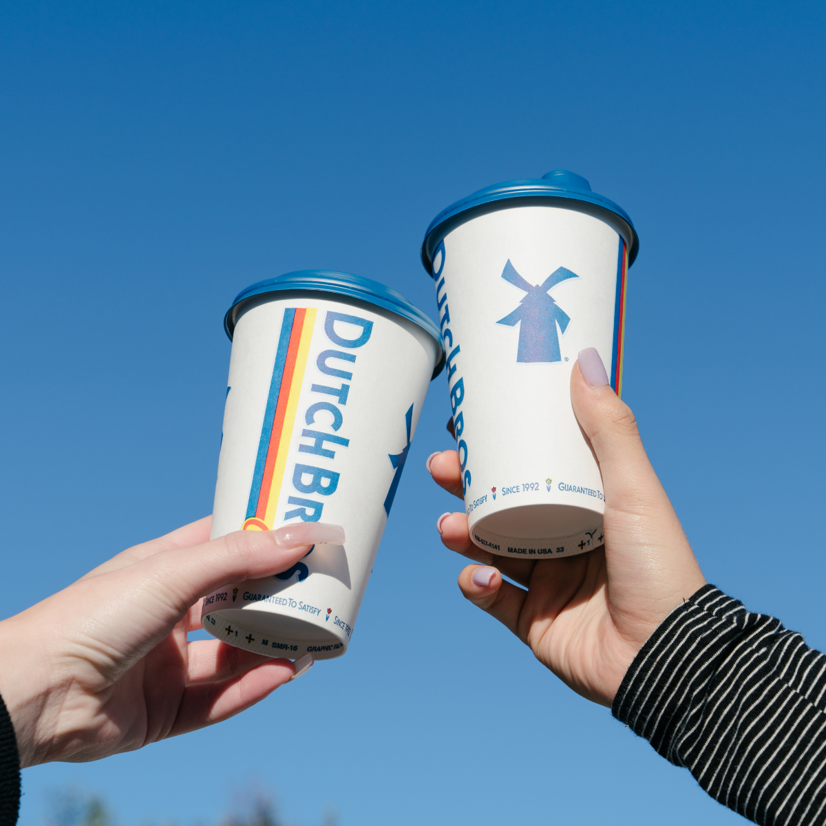 two coffee cups being held by two hands in air